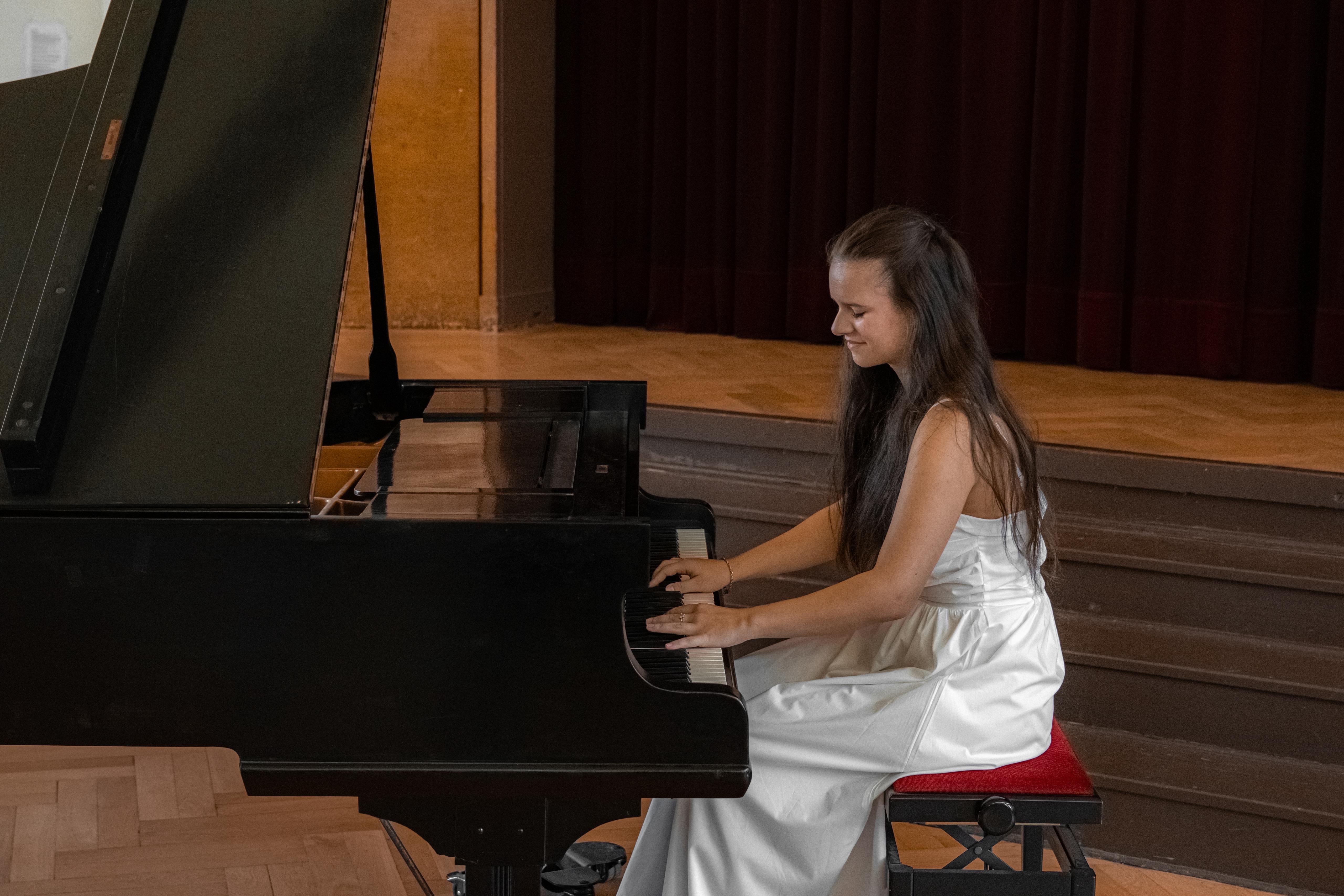 Frau in weißem Kleid sitzt am Klavier auf einer Bühne und spielt Musik