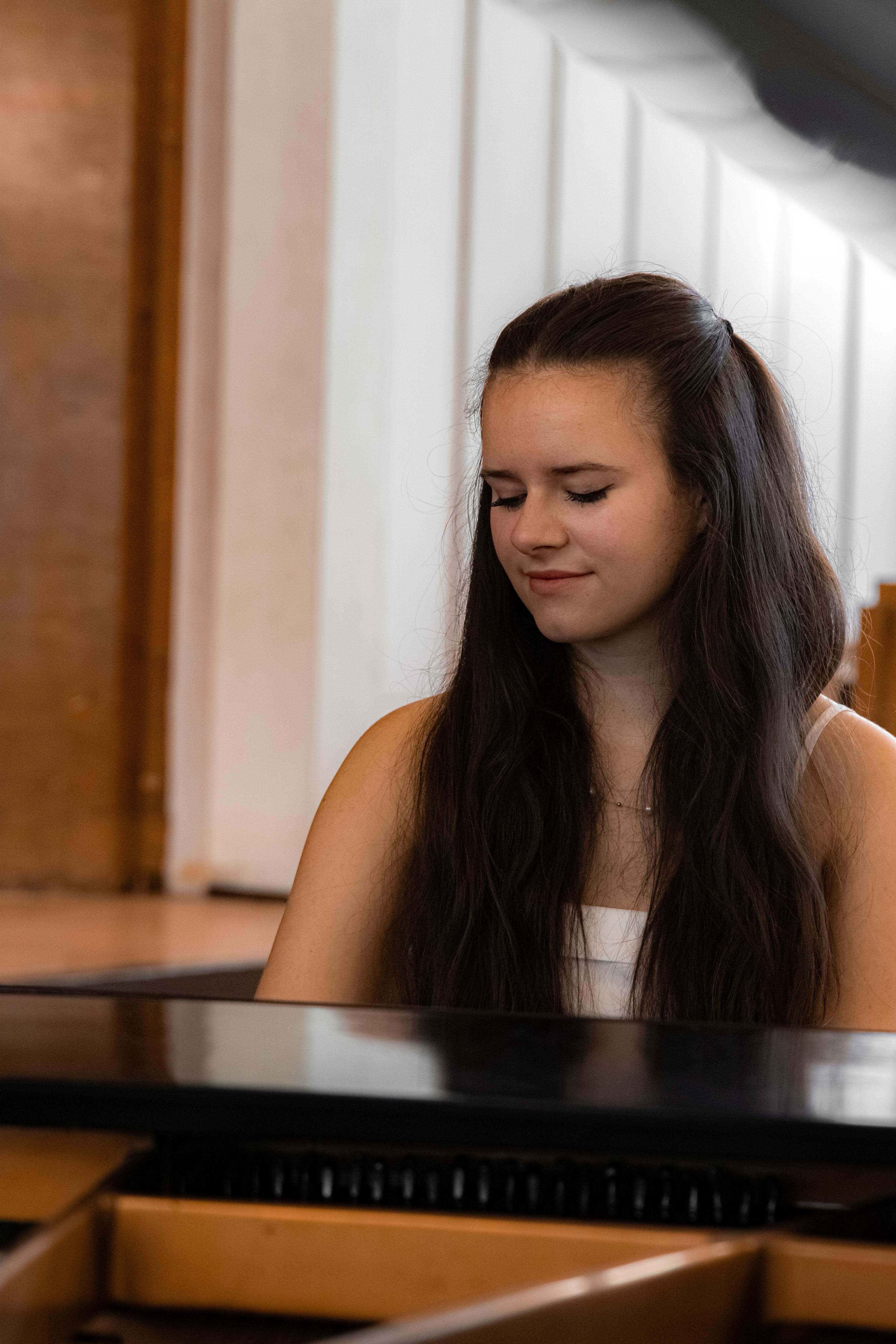 Eine junge Frau im weißen Oberteil spielt konzentriert Klavier.