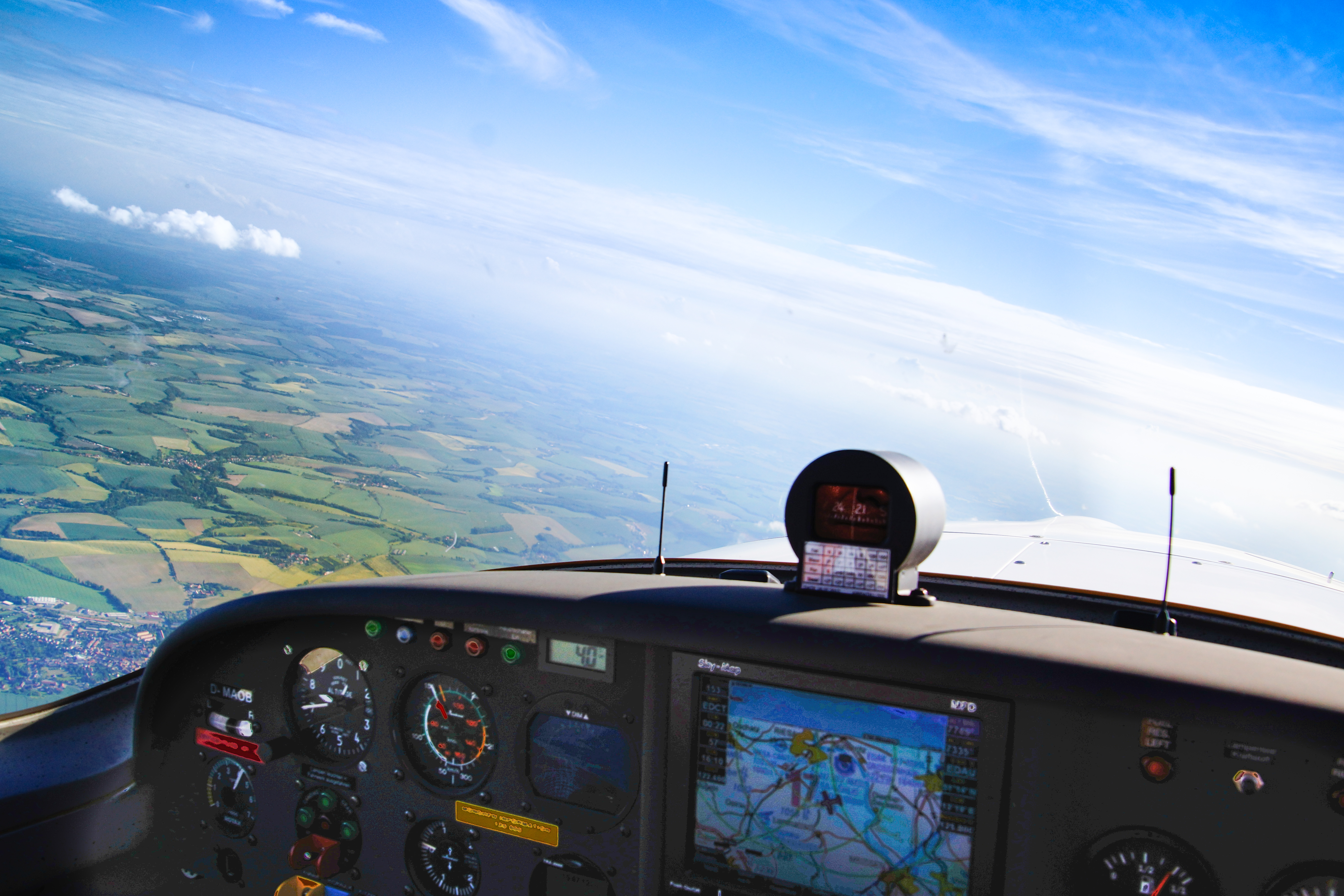 Blick aus dem Cockpit eines Kleinflugzeugs, das über eine grüne Landschaft fliegt