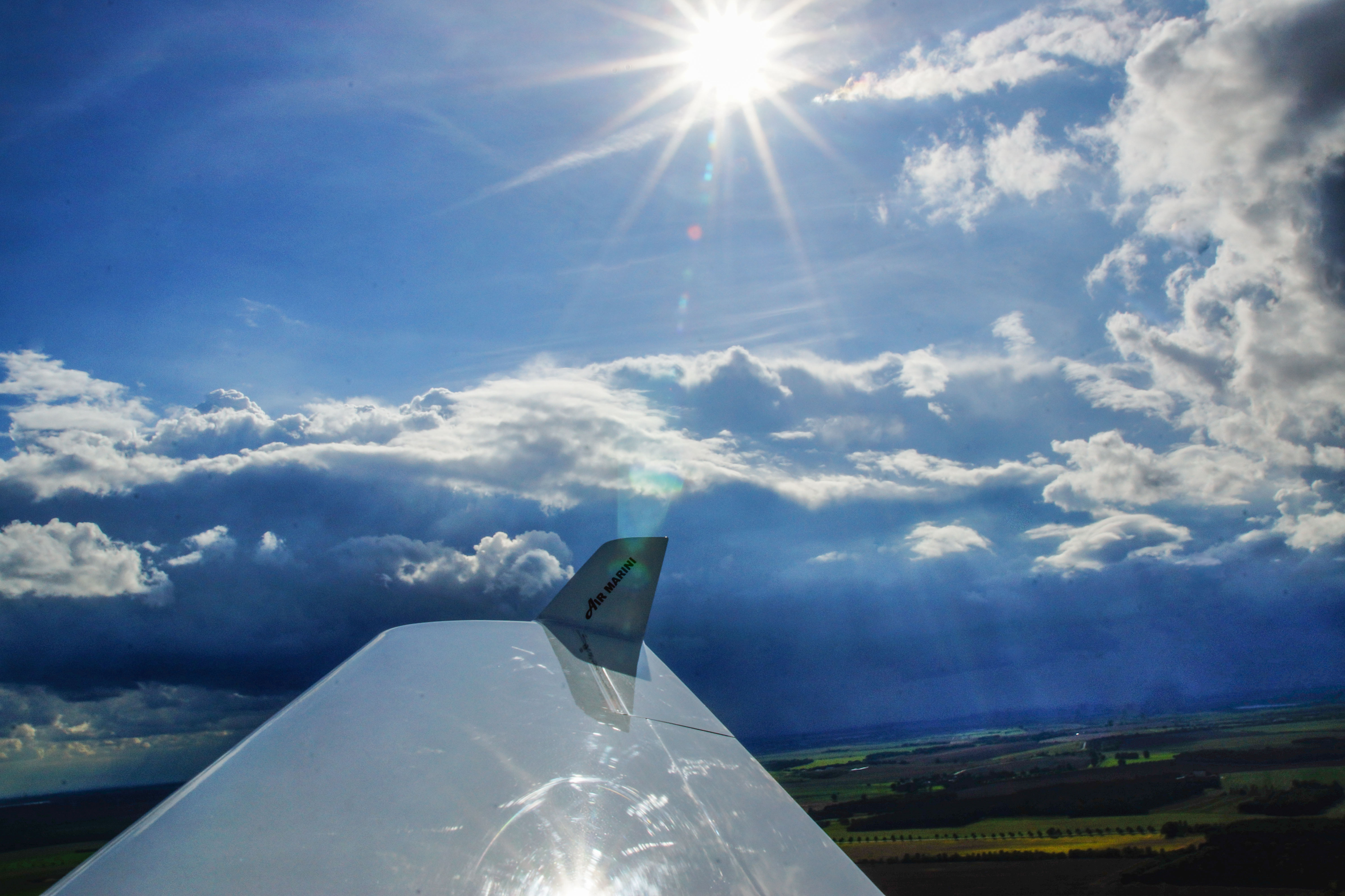 Flugzeugflügel im Vordergrund mit sonnigem Himmel und Wolken im Hintergrund