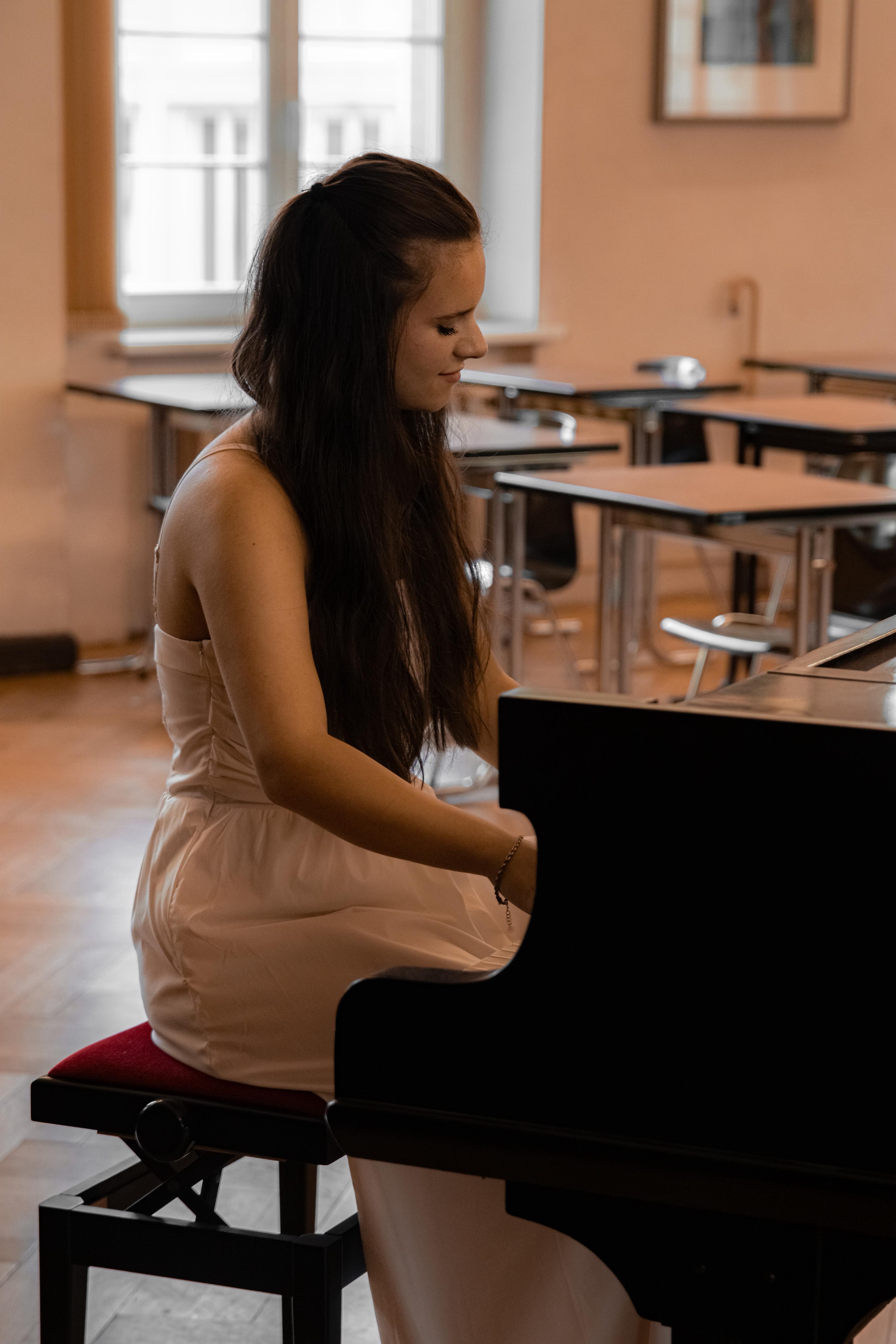 Junge Frau in einem weißen Kleid sitzt an einem Klavier und spielt Musik in einem Raum mit Holzmöbeln