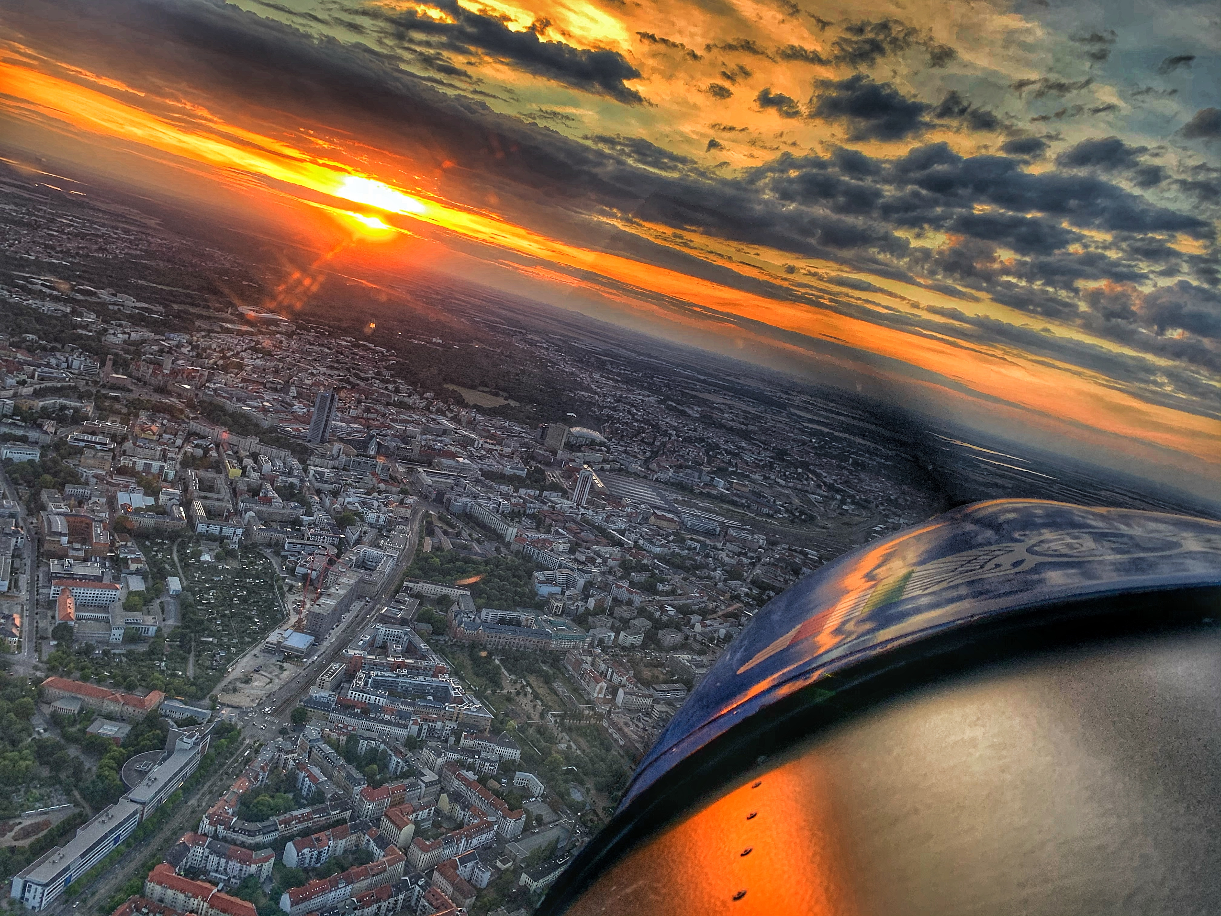 Blick aus einem Flugzeug auf eine Stadtlandschaft bei Sonnenuntergang mit dramatischem Wolkenhimmel