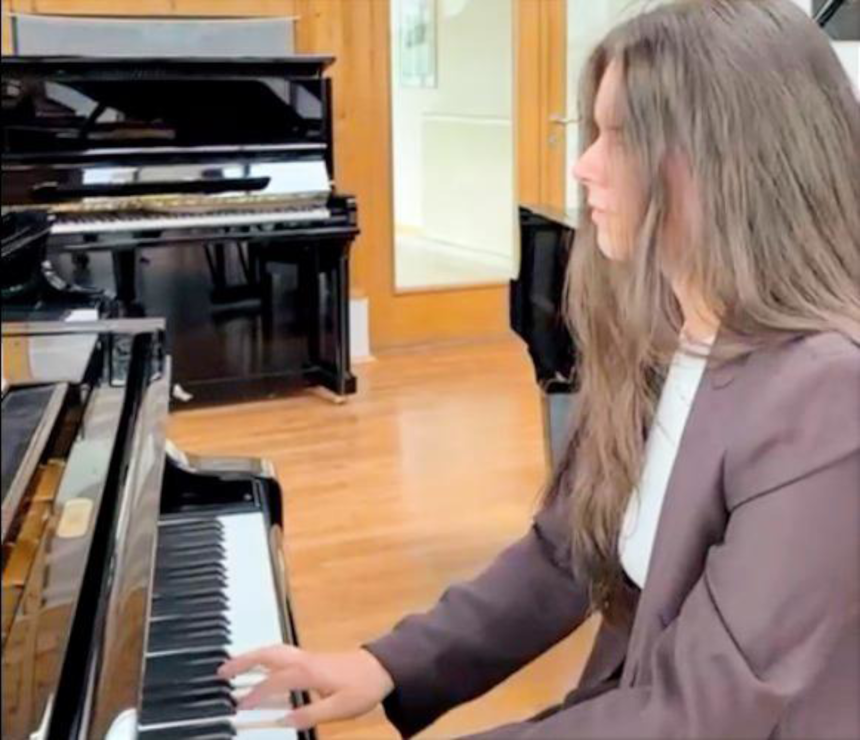 Seitenansicht einer Frau mit langen Haaren, die in einem Musikraum ein Klavier spielt