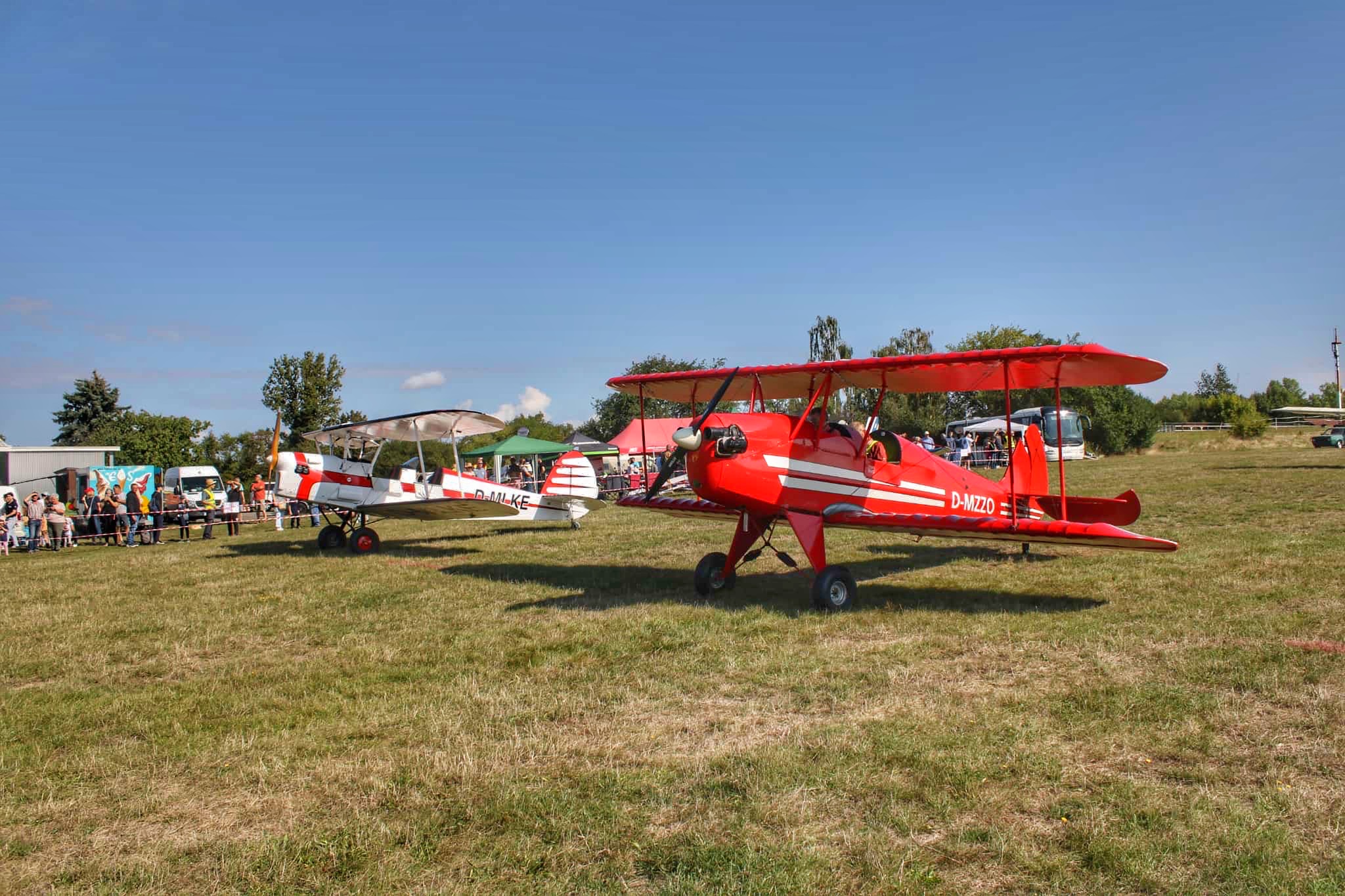 Zuschauer bestaunen zwei historische Doppeldecker-Flugzeuge auf einer grünen Wiese während einer Flugschau