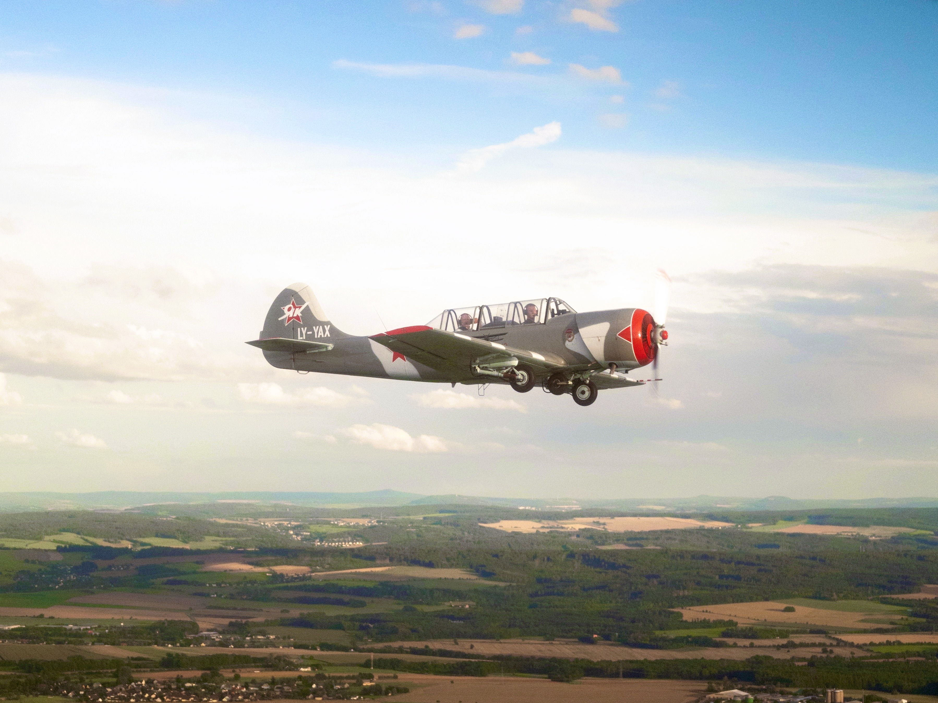 Altes Propellerflugzeug fliegt am Himmel über Feldern