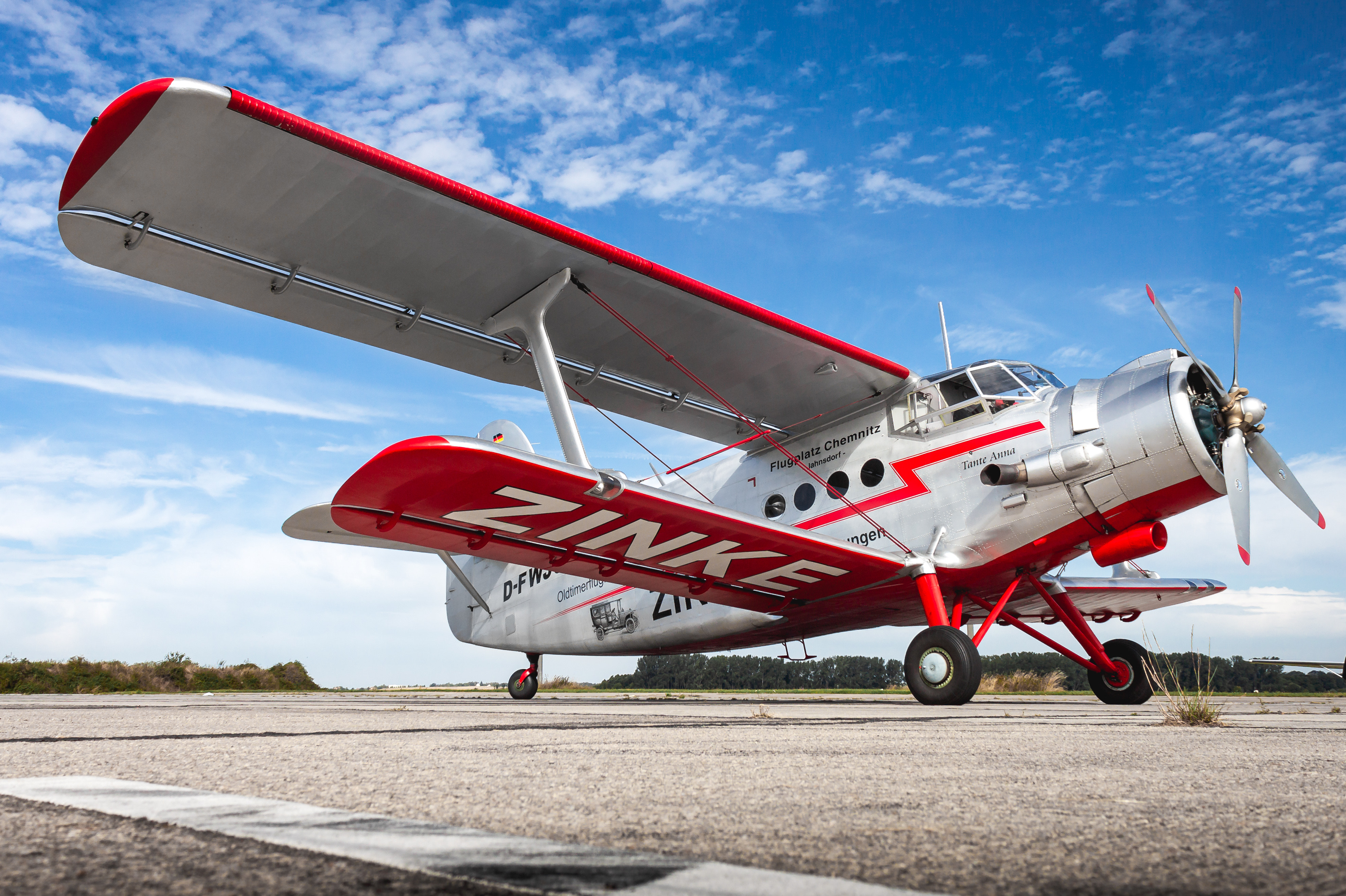 Seitenansicht eines roten und silbernen Doppeldeckers auf einem Flugplatz mit klarem Himmel