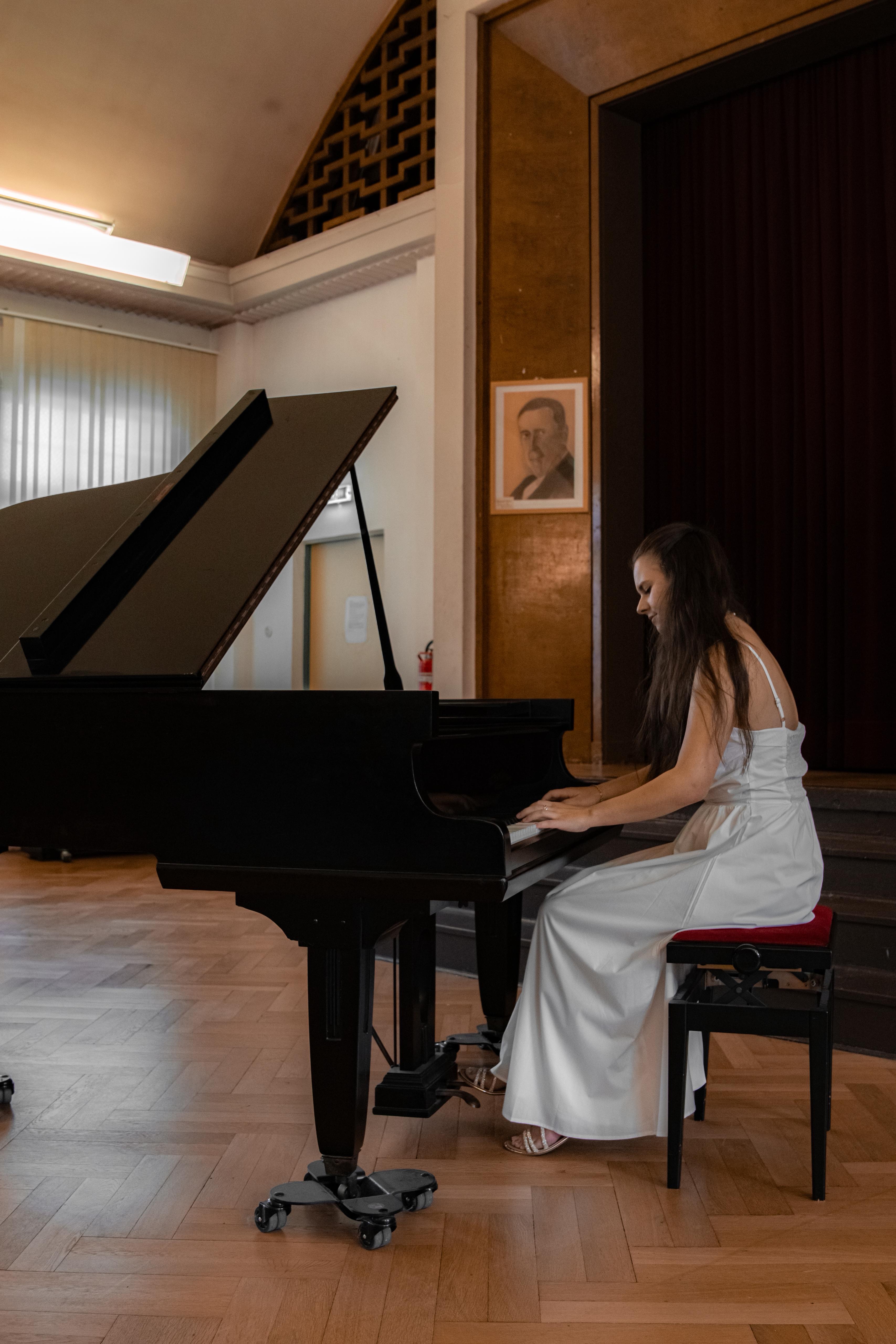 Junge Frau in weißem Kleid spielt Klavier auf einer Bühne in einem Konzertsaal