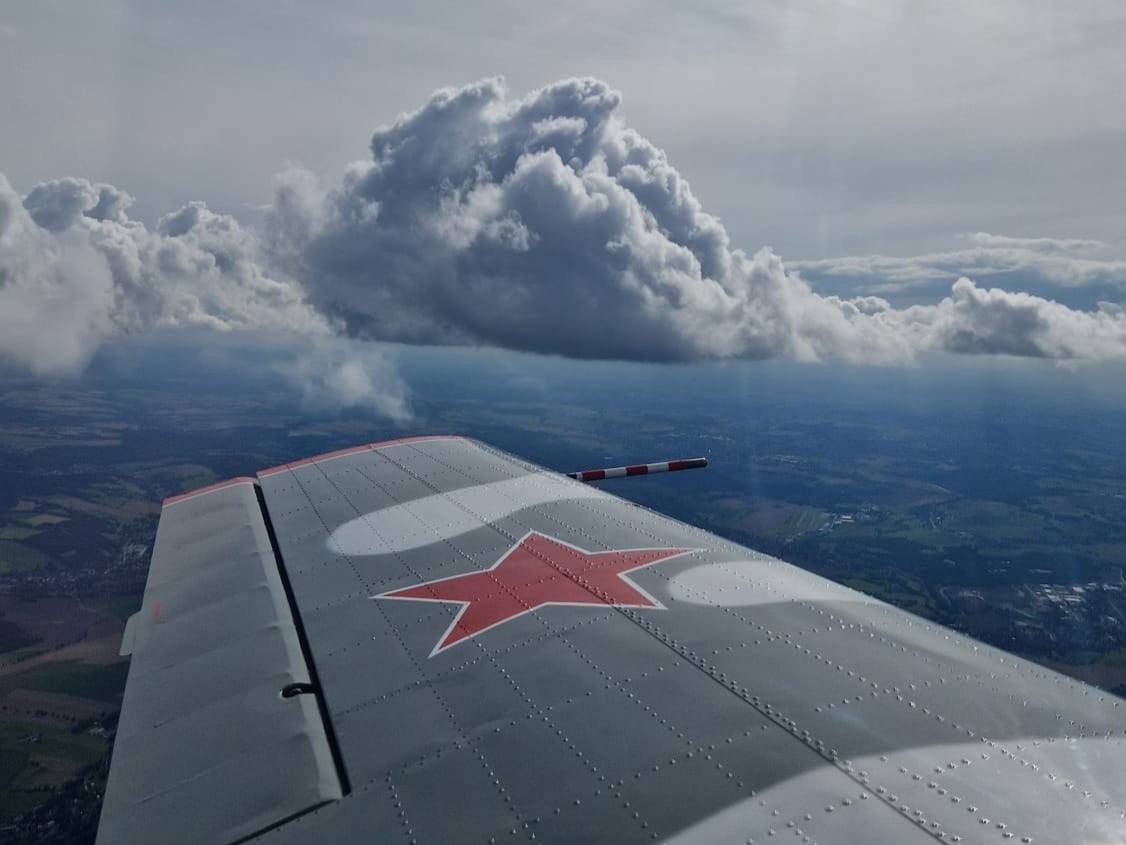 Flugzeugflügel mit rotem Stern vor Wolken und Landschaft
