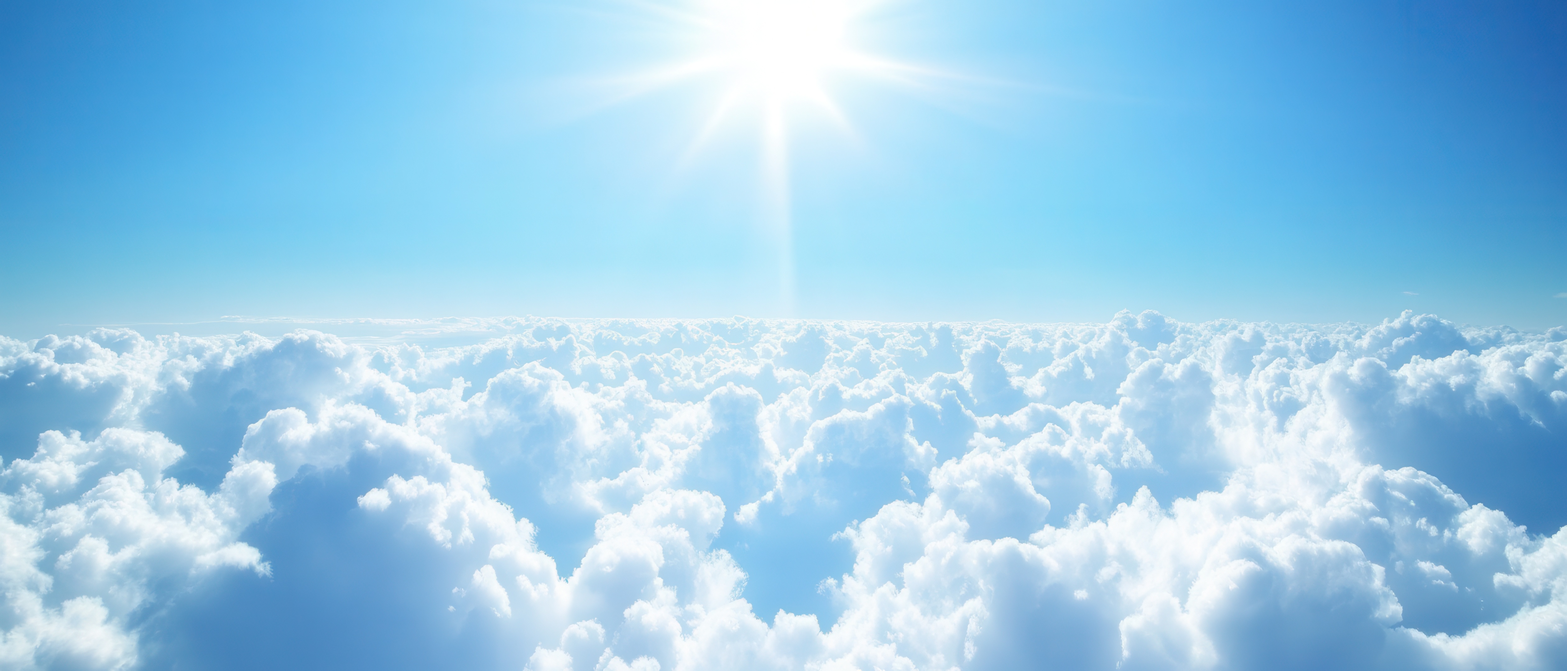 Ein strahlend blauer Himmel mit der Sonne, die über einer weiten Wolkendecke erscheint